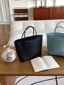 Detailed close-up of woven straw tote bags in black and light blue on a wooden table
