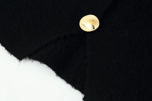 Macro detail of high-quality black knit fabric featuring a polished gold metal button