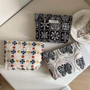 Three-piece embroidered makeup pouches with floral patterns on a minimalist tabletop