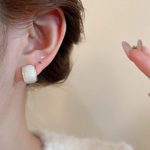 Detail shot of geometric pearl stud earring with gold metal trim on model ear