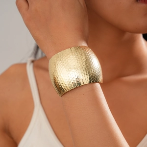 Close-up of a wide hammered texture golden metal open cuff bracelet worn by a model