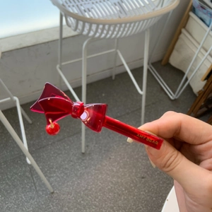Detail of a red acetate bow hair clip with a round charm and gold lettering accents