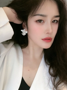 Close-up of a model wearing a silver ruffled flower earring with a polished metal finish
