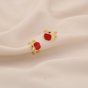 Detailed view of red and green enamel apple ear cuff on beige fabric background