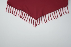 Detailed macro view of dark red fabric edge with decorative beaded fringe tassels