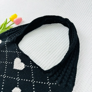 Detail of black knitted tote bag featuring white heart patterns and woven texture