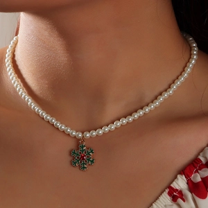 Detailed close-up of a pearl necklace featuring a green snowflake pendant and a red gem