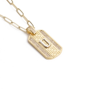 Détail d'un pendentif hip hop en or avec texture tissée, zircons et lettre U en argent