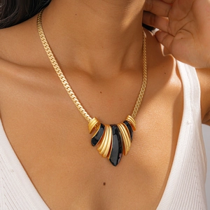 Detail of chunky gold snake chain necklace with layered black enamel wave pendant on a model