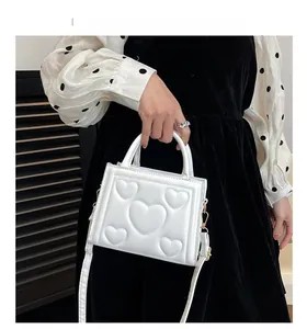 Vue détaillée du sac à bandoulière en cuir blanc avec motif cœurs gaufrés et boucles dorées