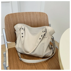Detail view of the creamy white leather tote bag featuring rivet accents on a wooden chair