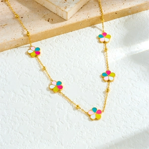 Detail of golden choker chain with multi-colored enamel flower charms on stone surface