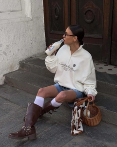 Detailed view of white half-zip sweatshirt paired with tall leather boots on steps