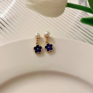 Detailed close-up of blue enamel flower earrings with pearl accents on a white dish