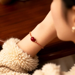 Detail eines Armbands mit roter Perle und Goldblatt an einem gemütlichen Strickpullover