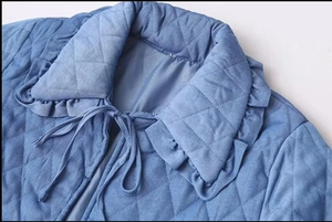 Detail view of a light blue quilted jacket featuring diamond patterns and a ruffle collar