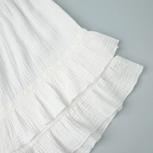 Dettaglio del tessuto in crepe bianco con pizzo delicato e trama dell'orlo a balze