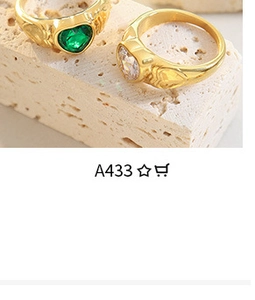 Detailed shot of gold textured rings with green heart and clear round gemstones on stone