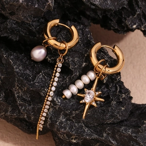 Macro detail of asymmetric gold earrings with pearls and zircon star on black stone