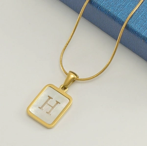Detail of 18K gold snake chain with a rectangular white shell letter H pendant