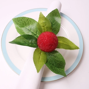 Detail view of red faux berry napkin ring with green leaves on a white linen napkin