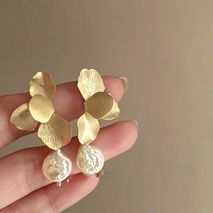 Detailed close-up of golden brushed flower petal earrings with baroque pearl drops