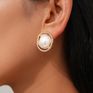 Close-up of a golden earring featuring a large central pearl and double rhinestone halo