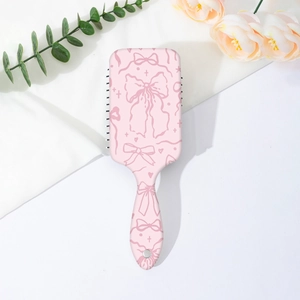 Flat lay of pink air cushion hairbrush with white bow pattern and floral decoration