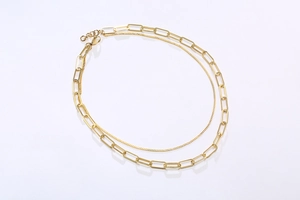 Detailed view of golden layered paperclip and curb chain necklace on white background