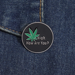 Macro shot of a black enamel pin with a green leaf and text on blue denim fabric