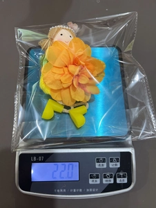 Detailed view of an orange flower doll pendant weighing 22.0g on a digital scale