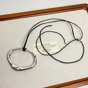 Detail of silver irregular ring pendant on black cord over a white fabric background
