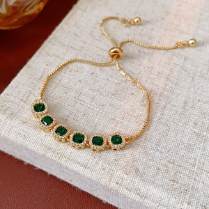 Close-up of golden box chain bracelet featuring six square green zircons with halo diamonds