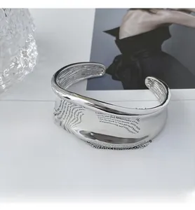 Macro shot of silver wide irregular wavy open cuff bangle on a white editorial background