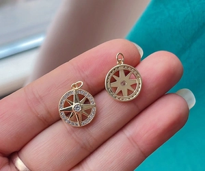 Macro shot of gold compass charms featuring pavé cubic zirconia and hollow metal designs