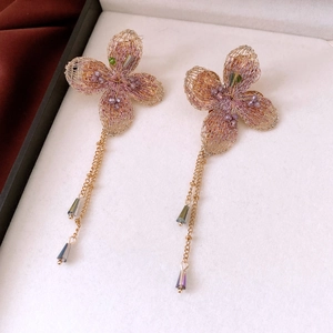 Close-up of handmade golden woven flower earrings with purple beads and drop pendants
