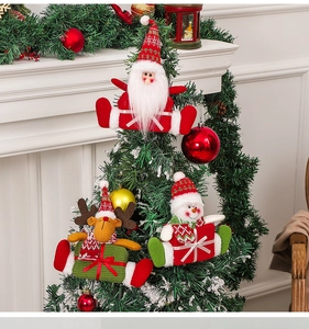 Detail of plush Santa and reindeer knit ornaments hanging on a green Christmas tree