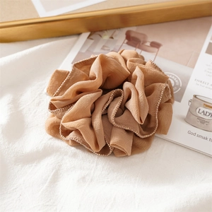 Detail of beige scrunchie with gold bead edging on a minimalist white texture background