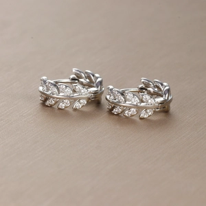 Silver olive leaf hoop earrings with shimmering crystals on a textured brown base