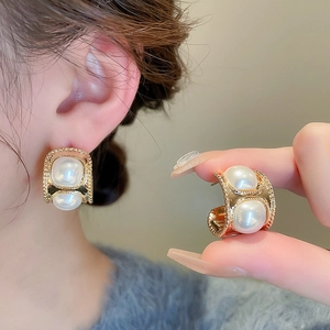 Boucles d'oreilles vintage en C dorées avec perles nacrées sur fond de pull bleu marine