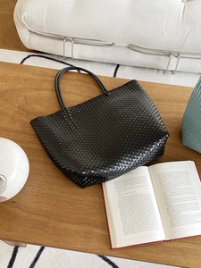 Handwoven black straw tote bag with dual handles on a wooden table for summer travel