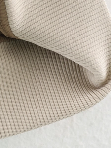 Detailed close-up of beige ribbed knit tweed jacket fabric with dark brown piping trim