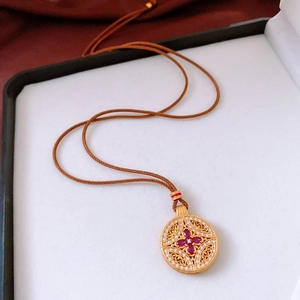 Detail of vintage round pendant with red gems and zircon filigree on brown cord