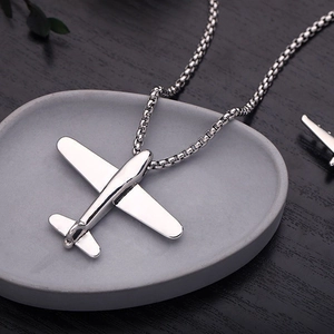 Macro shot of a silver metal airplane pendant with a sleek box chain on a grey tray