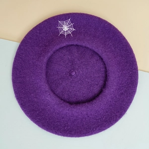 Top view of dark purple wool beret with white spider web embroidery detail