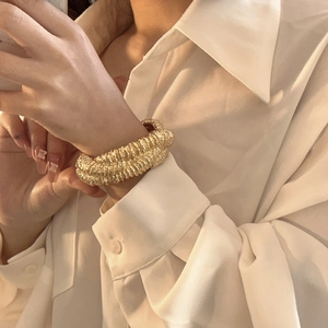 Close-up of golden irregular textured cuff bracelet on woman's wrist in white shirt