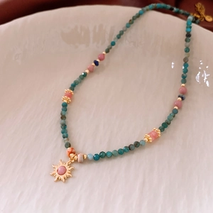 Detailed close-up of beaded sun pendant necklace on a textured ceramic plate