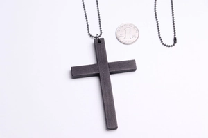 Detailed view of the black cross necklace showing size reference with a coin on white