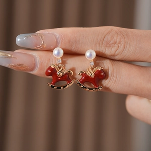 Macro view showing a red rocking horse earring with gold wings and a white pearl accent