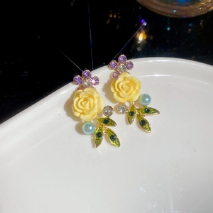 Detail of vintage floral earrings with yellow roses, green leaves, and pearls on a white plate